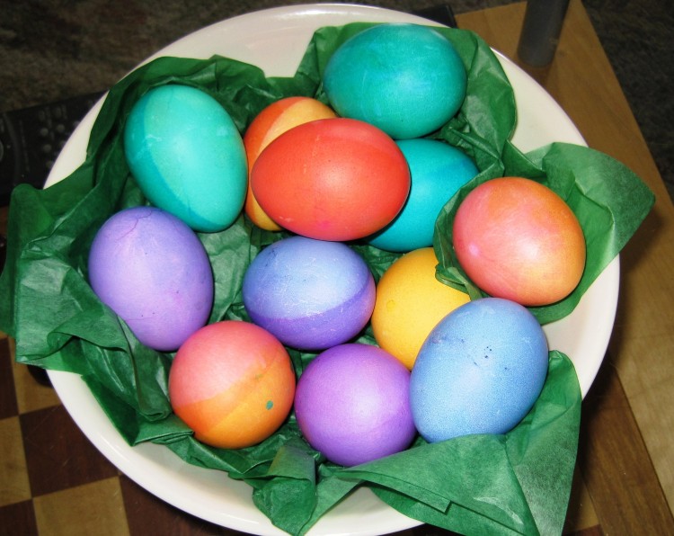 Plate of easter eggs in multiple colors in white bowl with green tissue paper